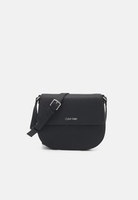 Sort crossbody-taske med klaplåge, lavet af tekstureret materiale. Har en justerbar rem og en sølvfarvet logo foran.
