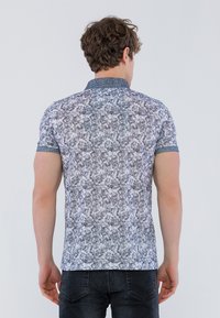 Polo a maniche corte con un motivo floreale blu e bianco, dettaglio del colletto e design aderente, realizzato in un tessuto testurizzato.