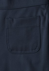 Tissu bleu foncé avec une poche plaquée carrée cousue, montrant des détails de couture visibles sur un matériau lisse.