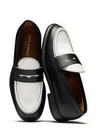 Zwart-witte leren loafers met een gladde textuur, voorzien van een verhoogde zwarte band en stikdetails. Rond neus en platte hak.