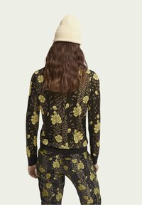 Suéter negro con un patrón floral amarillo, manga larga y puños acanalados. Combinado con pantalones a juego, creando un look coordinado.