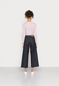 Pruhovaný dlouhý rukáv top v levandulové a bílé barvě, vysoké tmavé džíny s širokými nohavicemi a bílé platformové tenisky.