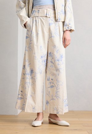 Παντελόνια σε μπεζ χρώμα με φαρδιά πόδια και ανοιχτομπλε floral σχέδιο, με ζώνη στη μέση που ταιριάζει, συνδυασμένα με εκρού slingback flats και κοντό σακάκι.