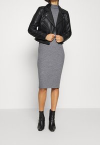 Veste de moto en cuir noir sur une robe midi à côtes grise, assortie à des bottines noires. Texture lisse, design ajusté et silhouette structurée.