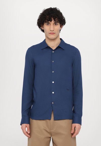 Chemise à manches longues bleu marine en tissu lisse, dotée d'un col à boutons, de boutons sur le devant et d'un petit logo brodé.