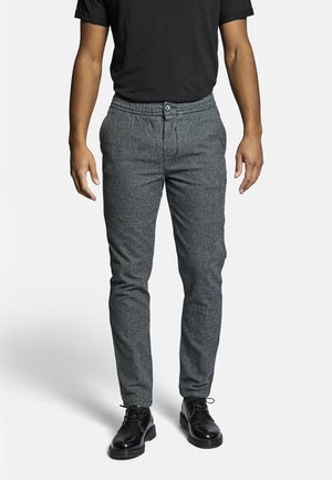 Pantalons gris texturé avec taille à cordon de serrage et fermeture à bouton, associés à des chaussures habillées noires et un t-shirt noir basique.