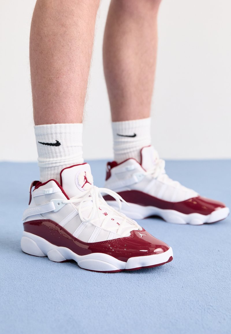 Baskets de sport blanches et bordeaux avec des accents en cuir verni brillant, des panneaux en mesh et des lacets blancs. Semelles blanches épaisses et structure de soutien pour la cheville.
