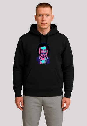 Man wearing black hoodie with neon-colored smiling man's face graphic, paired with light gray sweatpants, standing against plain background.