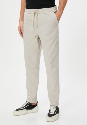 Lys beige bukser med elastisk talje og snøre. Har to frontlommer, tapered fit og flade sømme for et rent design.