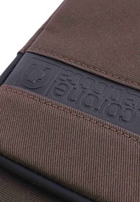 Primer plano de una tela marrón con costuras texturizadas y una etiqueta de goma negra grabada con "Coronado Polartec" y un logo de corona.