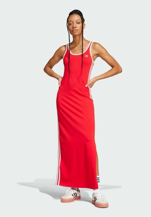 Red maxi dress with white tank straps, featuring side slits and three white stripes along the sides. Pair of white sneakers with stripes.