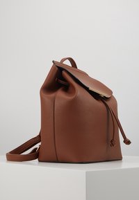 Zaino in pelle marrone con finitura texturizzata, chiusura con gancetto in oro e chiusura a coulisse. Il design è minimalista e strutturato.