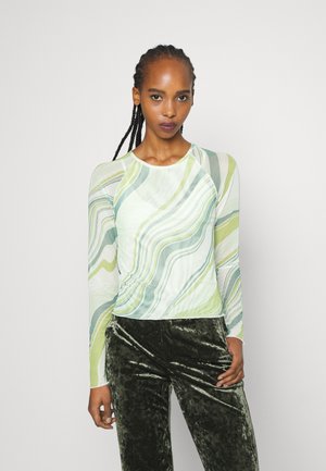 T-shirt de manga longa com um padrão em mármore verde, branco e azul claro; tecido leve e texturizado; combinado com calças de veludo verde escuro.