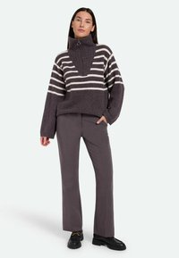Pull rayé gris et crème avec col montant, doté d'une fermeture éclair. Associé à un pantalon droit gris et des chaussures noires.