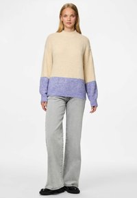 Pull en tricot crème et lilas, présentant une coupe décontractée, un col montant et des poignets côtelés. Associé à un jean évasé gris clair et des chaussures noires.