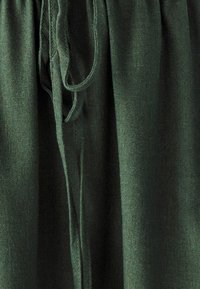 Tessuto verde con una texture morbida, dotato di chiusura con coulisse e design plissettato per una vestibilità regolabile in vita.