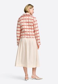 Blazer en tweed rouge et crème avec un motif à carreaux, fini avec des bords effilochés et des boutons, associé à une jupe midi crème pâle.
