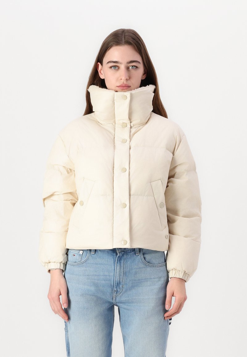 Veste matelassée courte en blanc cassé, avec un col haut, des boutons-pression et deux poches avant. Texture lisse avec un design épuré.