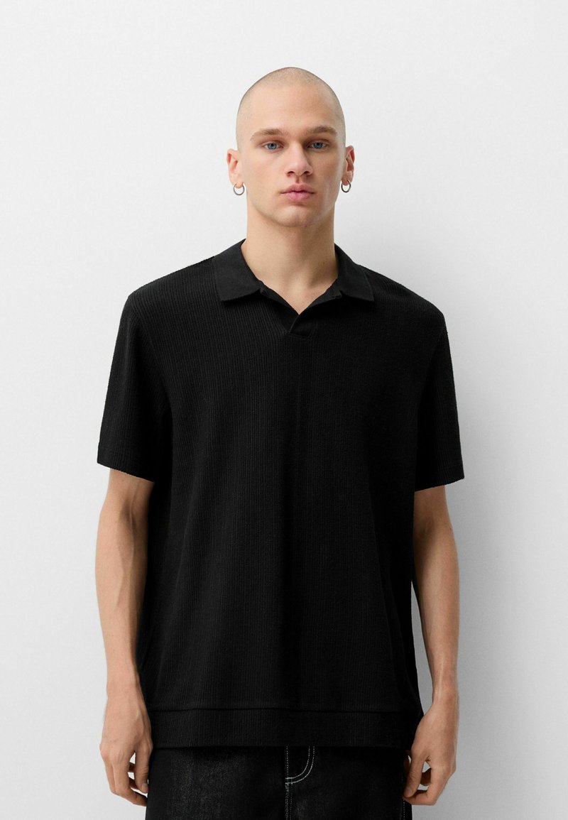 Polo shirt nera a maniche corte con un design a coste testurizzato, caratterizzata da un colletto e una vestibilità ampia. Stile semplice e minimalista.