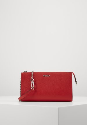 Sac pochette rouge Hugo avec finition texturée, bandoulière chaîne argentée et fermeture éclair, exposé sur un piédestal blanc sur fond uni.