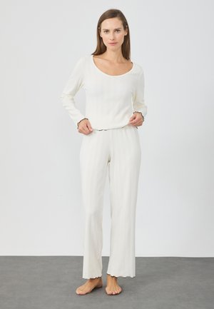Weißes Longsleeve-Oberteil und passende Hose mit gerippter Textur und gewellten Kanten. Das Material wirkt weich und leicht.