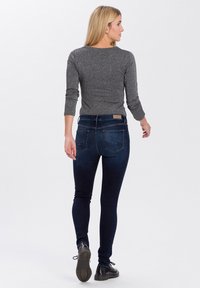 Slim-fit donkerblauwe jeans met vijf zakken, voorzien van een klassiek ontwerp en subtiele vervaging op de benen. Gekleed met een getailleerde grijze lange mouw top.