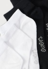 Svarta och vita strumpor staplade tillsammans; bomullsblandning med ribbad struktur. Vita strumpor har ljusgrå bokstäver, medan svarta strumpor har mörkare grå.