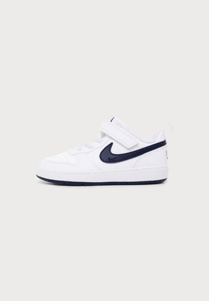Fehér sportcipő fekete Nike logóval, tépőzárral és fűzővel, oldalról fényes, egyszerű háttér előtt.