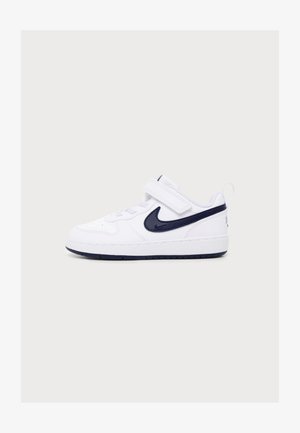 Baskets blanches avec le logo Nike noir, bride velcro et lacets, vues de côté sur un fond clair uni.