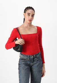 Karmiinpunane ribadest pikakä sleeves top, millel on ruudukujuline kaelus, koos kõrge vöökohaga siniste teksade ja väikese musta käekotiga.