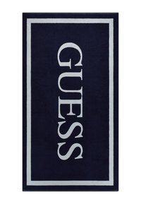 Navyblauer Teppich mit einem weißen rechteckigen Rand, der das Wort "GUESS" in großen, fetten weißen Buchstaben in der Mitte zeigt. Weiche Textur.