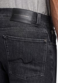 Zwarte spijkerbroek van denim met een leren taillebandlabel, een achterzak met gebogen stiksels en een metalen knoopaccent.