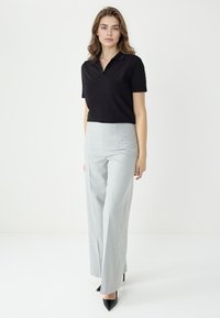 Zwarte polo met korte mouwen, gecombineerd met lichtgrijze wijde broeken met hoge taille en zwarte puntige hakken. Soepele stof, op maat gemaakte pasvorm.