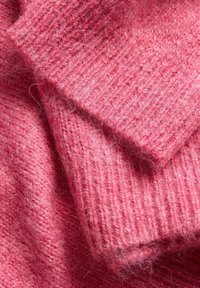 Gros plan d’un tissu tricoté rose doux et duveteux montrant une texture côtelée et des couches pliées.