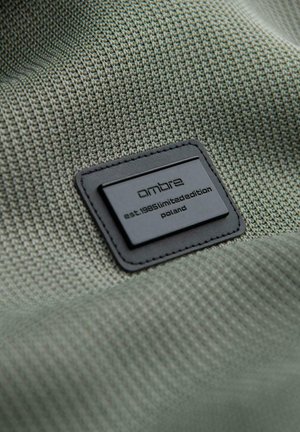 Schwarzes rechteckiges Ombré-Markenlabel auf strukturiertem grünem Stoff mit dem Aufdruck "est. 1985 limited edition Poland".