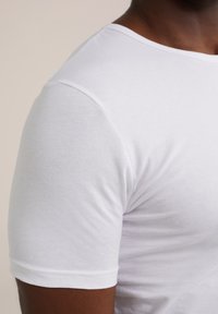 Witte korte mouwen t-shirt van lichtgewicht katoen, met een ronde hals en een gladde textuur, waarbij schouder- en armdetails zichtbaar zijn.
