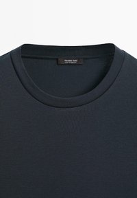 T-shirt crew neck di un blu navy scuro con un'etichetta nera visibile all'interno del colletto che recita "Massimo Dutti Made in Portugal."