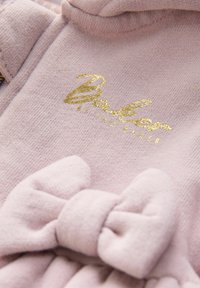 Mäkký ružový pletený detský komplet s veľkou látkovou mašľou a nápisom "Baby" napísaným zlatým kurzívou na hrudi.