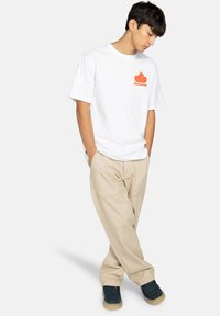 Biała bawełniana koszulka z pomarańczowym logo "Element" i wzorem liścia, w połączeniu z jasnobeżowymi spodniami cargo i ciemnymi butami. Slim fit, styl casual.