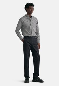 Sort og hvid gingham skjorte med knaplukning, parret med mørke bukser. Har krave, lange ærmer og en lige snitdesign. Sorte sko.