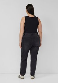 Schwarzes Tanktop kombiniert mit hoch sitzender, dunkelgrauer Jeans mit Gesäßtaschen und geradem Bein. Die Schuhe sind hell mit dunklen Akzenten.