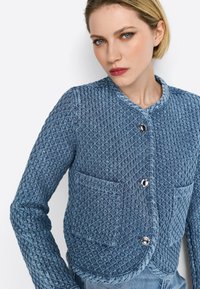 Giacca blu trapuntata con scollatura rotonda, chiusure a bottone argentato e due tasche frontali con texture a motivo diamante.