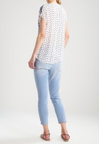 Lehká, krátká bílá blůza s navy puntíkovaným vzorem; v kombinaci se světle modrými, upnutými džíny a hnědými sandály.