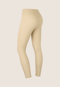Leggings beige con vita alta, tessuto liscio e design aderente. Presentano cuciture uniformi e taglio alla caviglia.