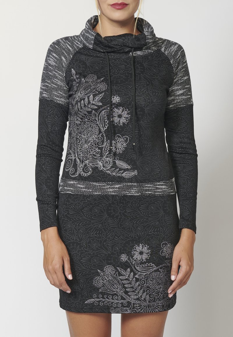 Robe noire à col bénitier, manches longues, avec des motifs floraux argentés. Présente des accents texturés noirs et gris sur les épaules.