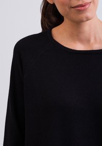 Schwarzer Pullover mit weitem Ausschnitt, langen Raglanärmeln und einer weichen Textur. Der Stoff wirkt leicht und glatt und eignet sich gut für legere Kleidung.