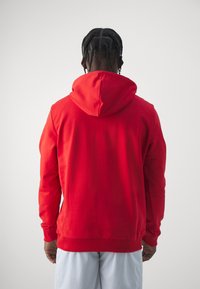 Red hoodie made of soft material, featuring a large hood, long sleeves, and ribbed cuffs and hem, view from the back.