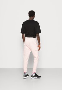 Svart oversized t-shirt, ljusrosa cargobyxor med sidofickor, resår i midjan och ribbade muddar, ihop med svarta och vita skor.