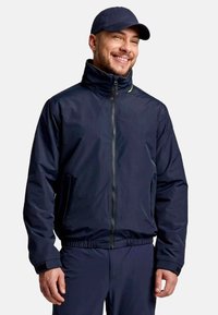 Giacca a vento blu navy con colletto alto, zip frontale e tasche laterali. Presenta polsini elasticizzati e un design slim fit.