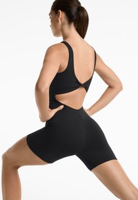 Black athletic bodysuit with a cutout back, featuring wide straps and a fitted design. Material appears smooth and stretchy.